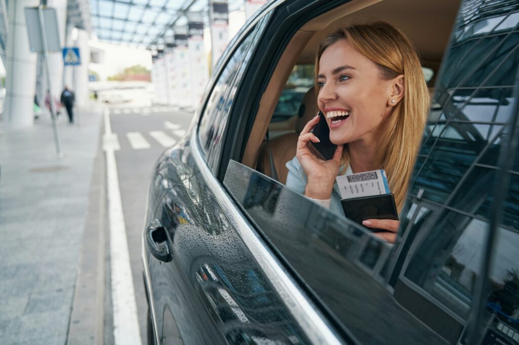 Cheerful passenger seated in car talking on smartphone
